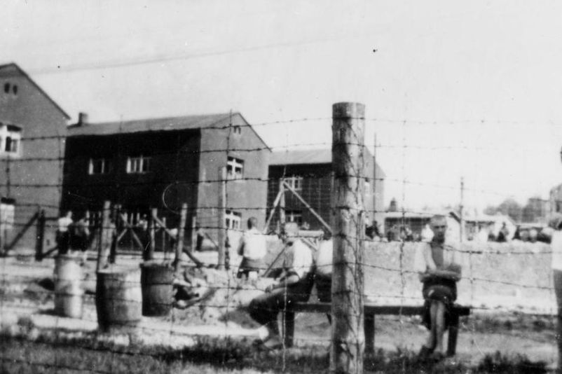 Blick aus dem westlichen Randbereich des Kleinen Lagers ins Hauptlager. Im Vordergrund sitzende bzw. stehende Häftlinge. Links im Bild die Steinblocks 46, 41 und 36.